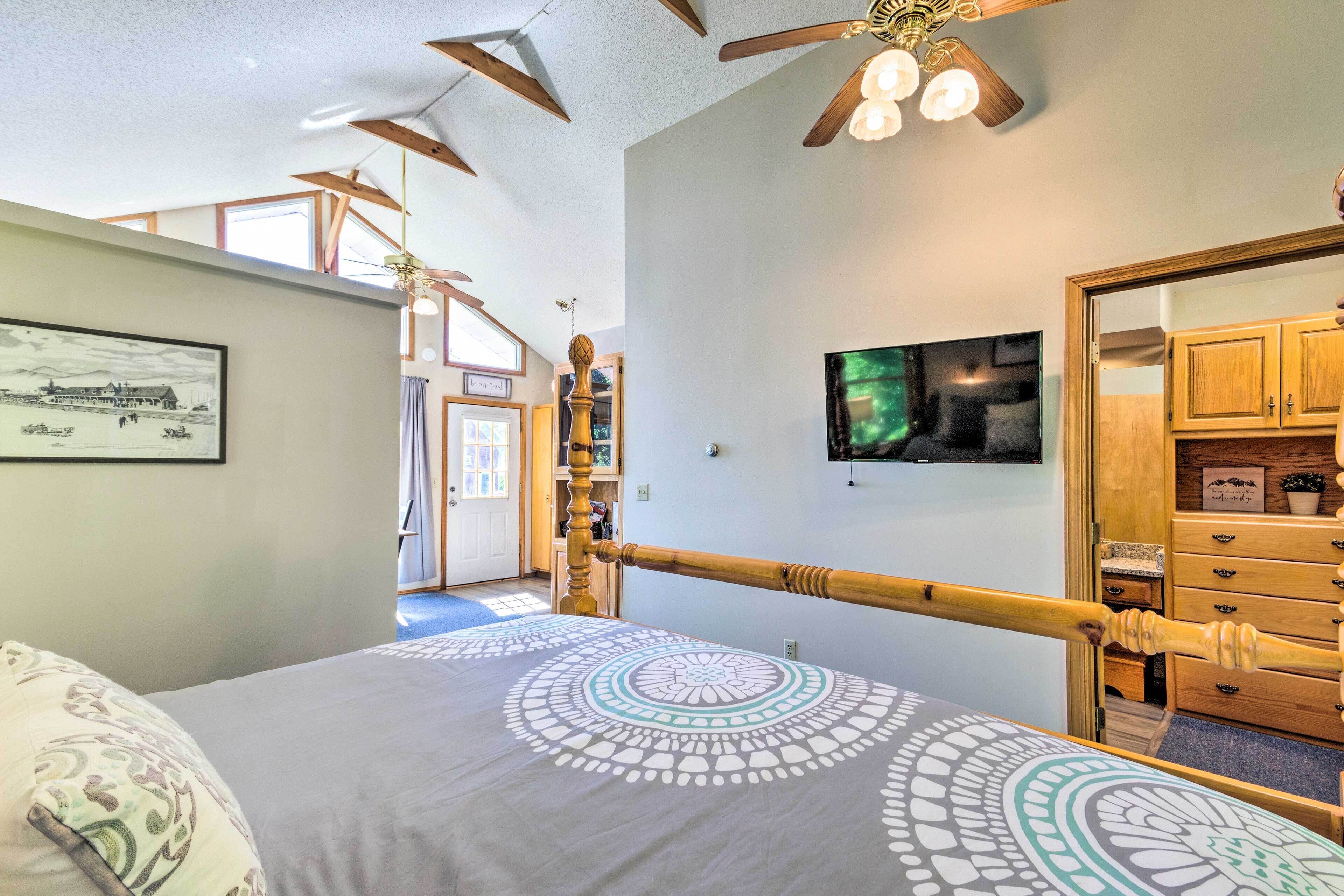 Une chambre à coucher comprenant un lit, un téléviseur, une commode en bois et un ventilateur de plafond.