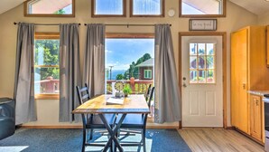 A room with a dining table, chairs, a clock, and a view of a house through a window. - Hendersonville 'cantrell Cottage' - Smoky Mtn View (Hendersonville)