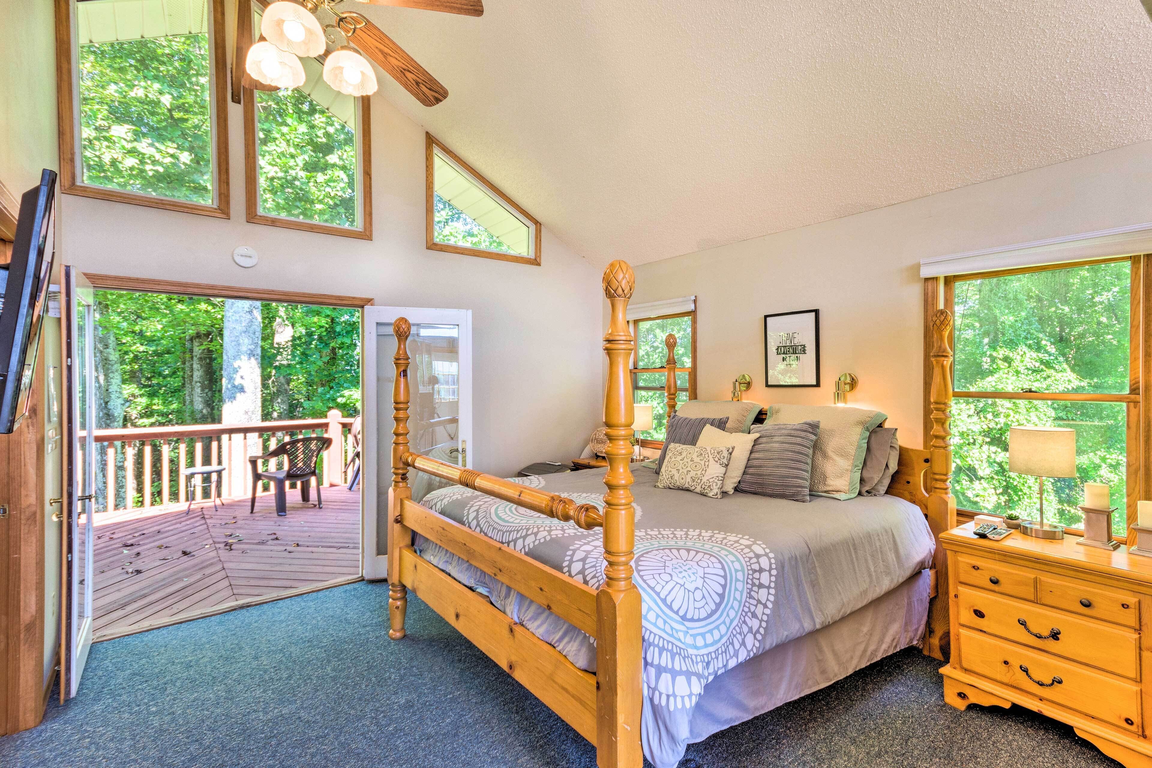 A bedroom with a wooden four-poster bed, a wooden nightstand, and a view of the outdoors through large windows.