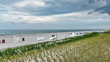 A beach with a lifeguard tower, a 'For Rent' sign, and a white building with red and blue accents.