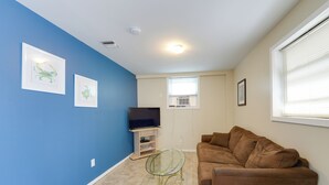 Ein Wohnzimmer mit blauer Wand, einem braunen Sofa, einem Glastisch und einem Flachbildfernseher auf einem Standfuß.