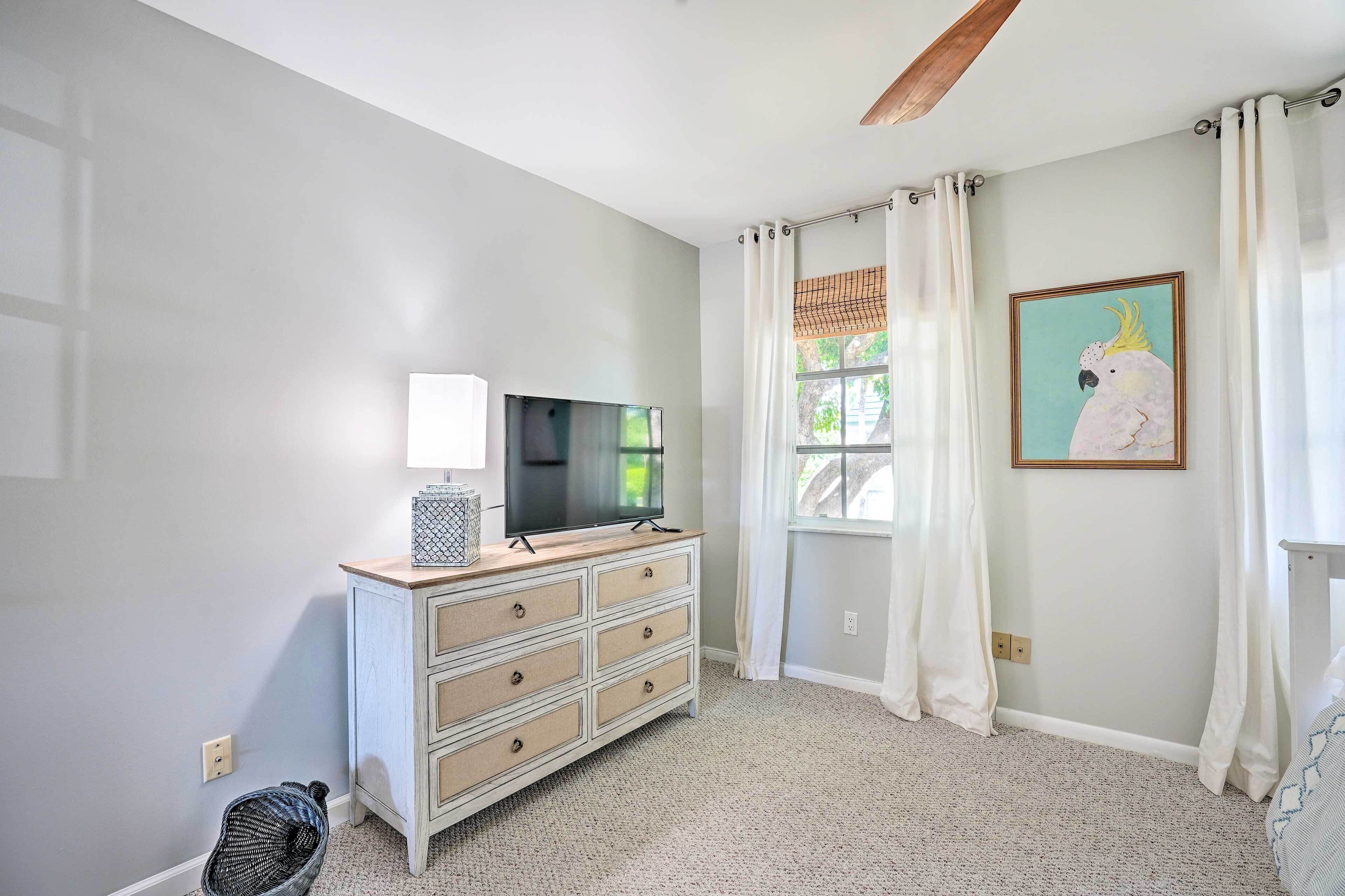 A room with a white dresser, a television, a framed artwork, and a window with curtains.