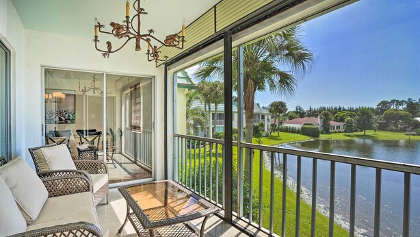 A balcony with wicker furniture, a glass table, and a view of a lake and greenery. - Relaxing Condo w/ Screened-in Lanai, 4 Mi to Beach (Naples)