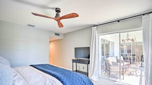 A bedroom with a bed, a ceiling fan, a TV, and a sliding glass door leading to a balcony with outdoor furniture. - Relaxing Condo w/ Screened-in Lanai, 4 Mi to Beach (Naples)