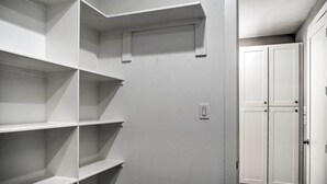 Un couloir étroit, avec des étagères blanches sur le côté gauche et une porte blanche sur le côté droit.
