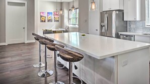 Une cuisine moderne avec des meubles blancs, des appareils en acier inoxydable et un îlot central doté de tabourets de bar.