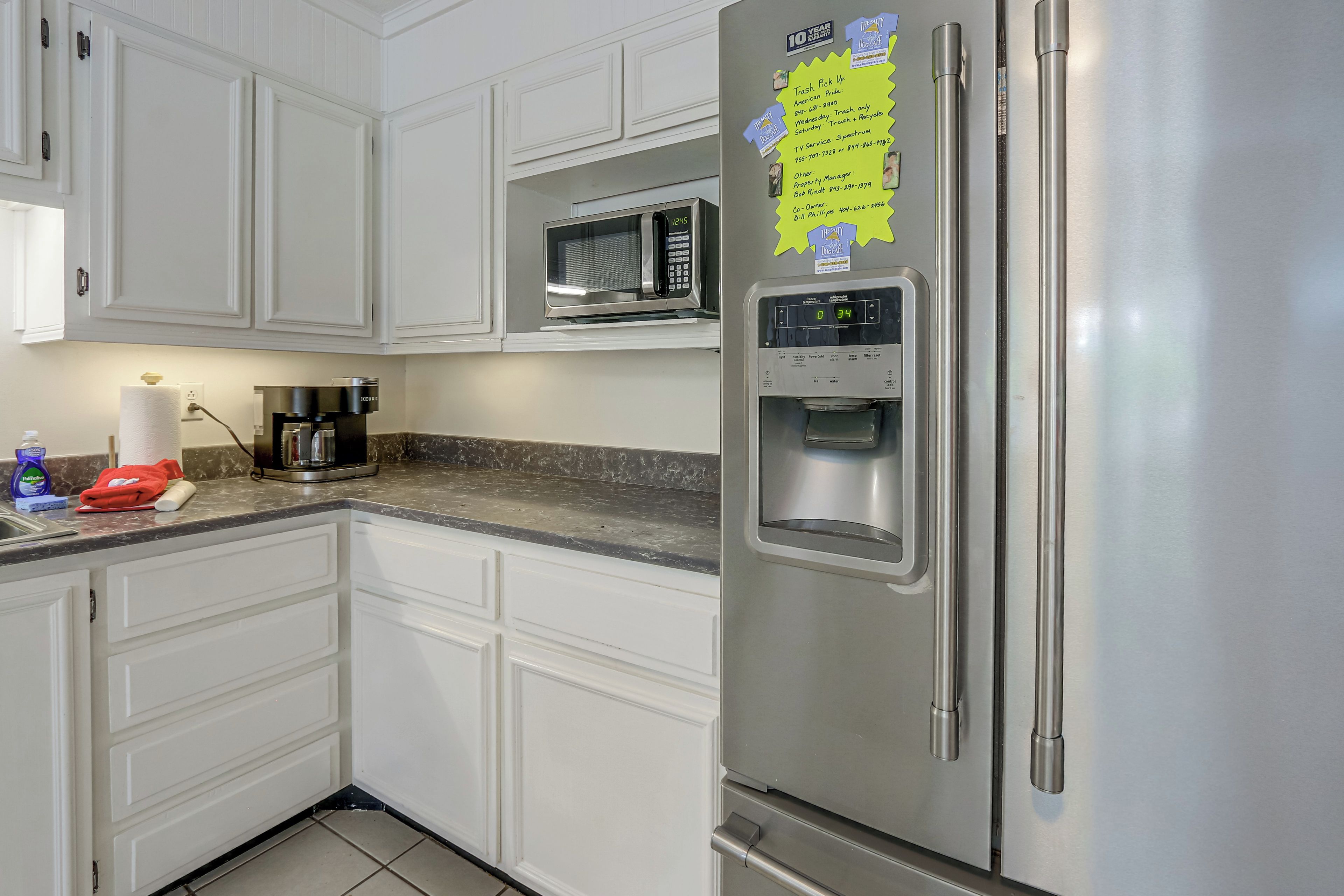 A kitchen with white cabinets, a stainless steel refrigerator, a microwave, and a coffee maker.