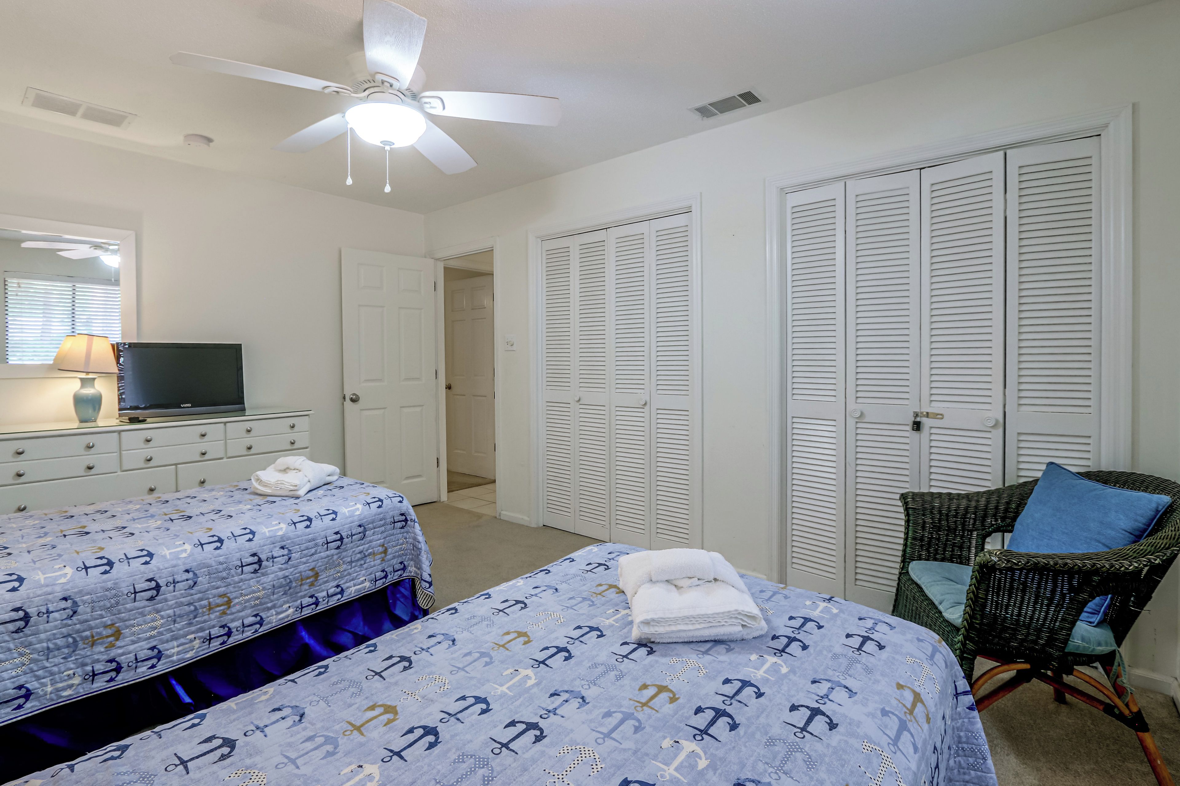 Une chambre avec deux lits, une télévision, un ventilateur de plafond et une chaise avec un coussin.