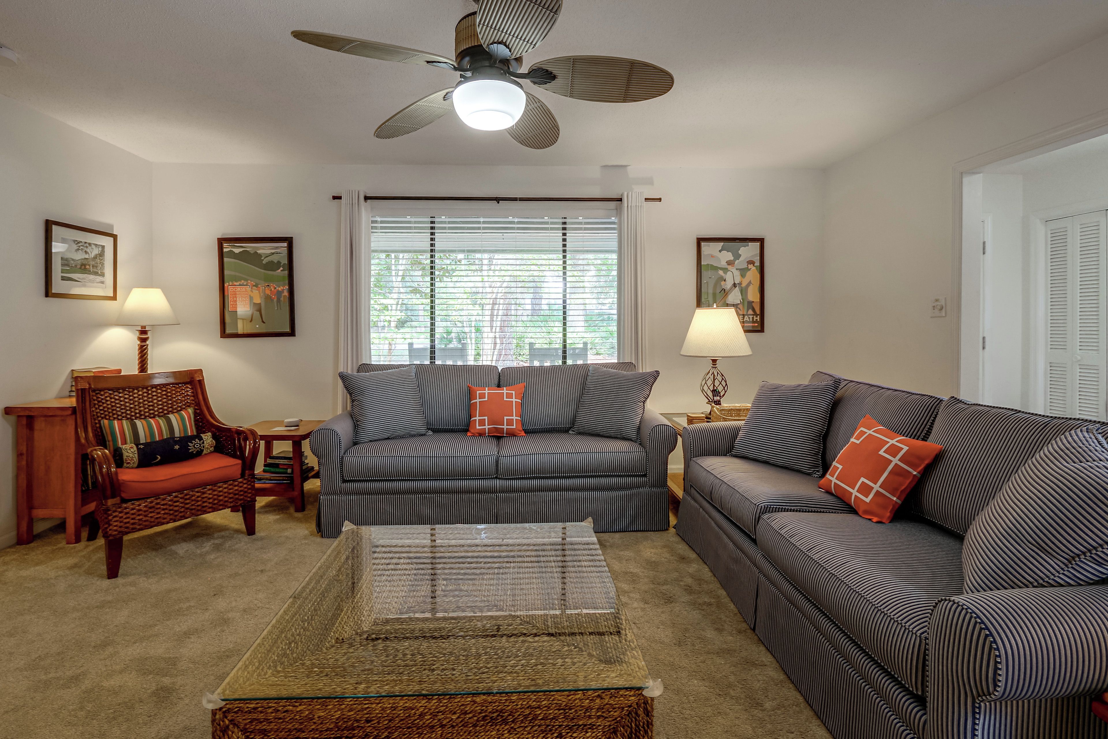 A living room with striped sofas, a wooden chair, a glass coffee table, and a ceiling fan.