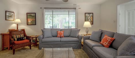 A living room with striped sofas, a wooden chair, a glass coffee table, and a ceiling fan.