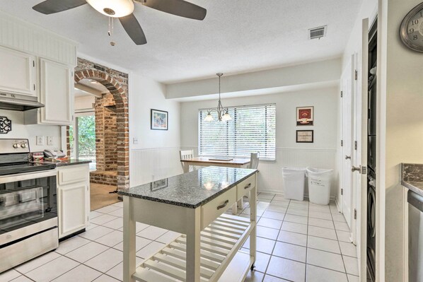 A kitchen with white cabinets, a brick archway, a granite countertop island, a ceiling fan, and a window with blinds. - < 1 Mi to Beach: Family-friendly Hilton Head Home (Hilton Head Island)