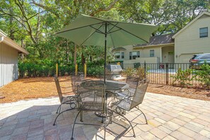Une terrasse avec une table et des chaises en métal, un parasol et un barbecue.