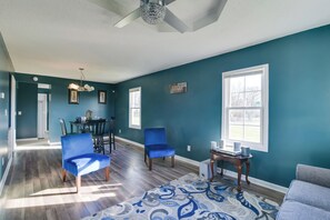 Una sala de estar con paredes azul verdoso, un tapete estampado y un comedor con sillas y una mesa.