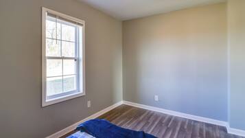 A room with a large window, wooden flooring, and a blue blanket on the bed.