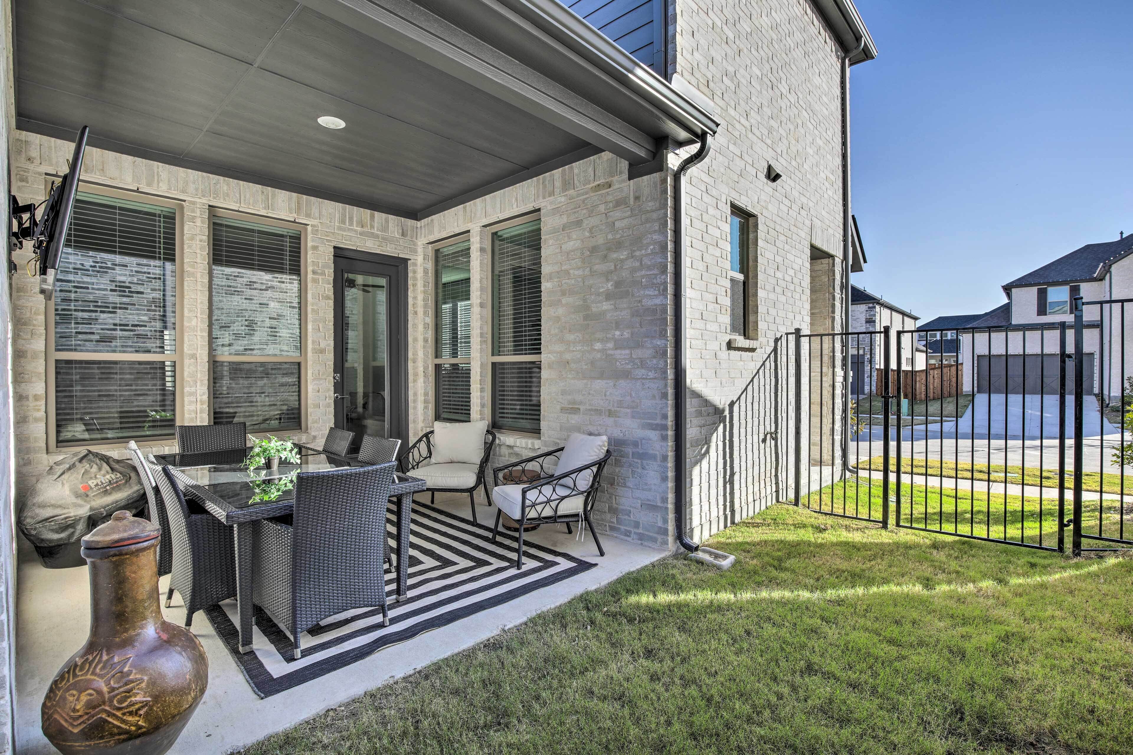 A covered patio with outdoor furniture, a large vase, and a brick exterior wall.
