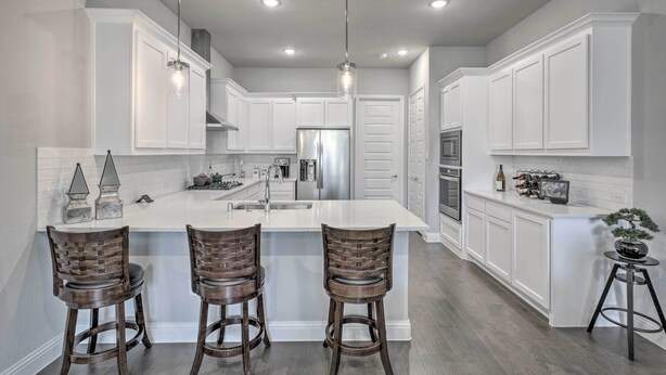 Una cocina moderna con armarios blancos, una isla central con taburetes, electrodomésticos de acero inoxidable e iluminación colgante.