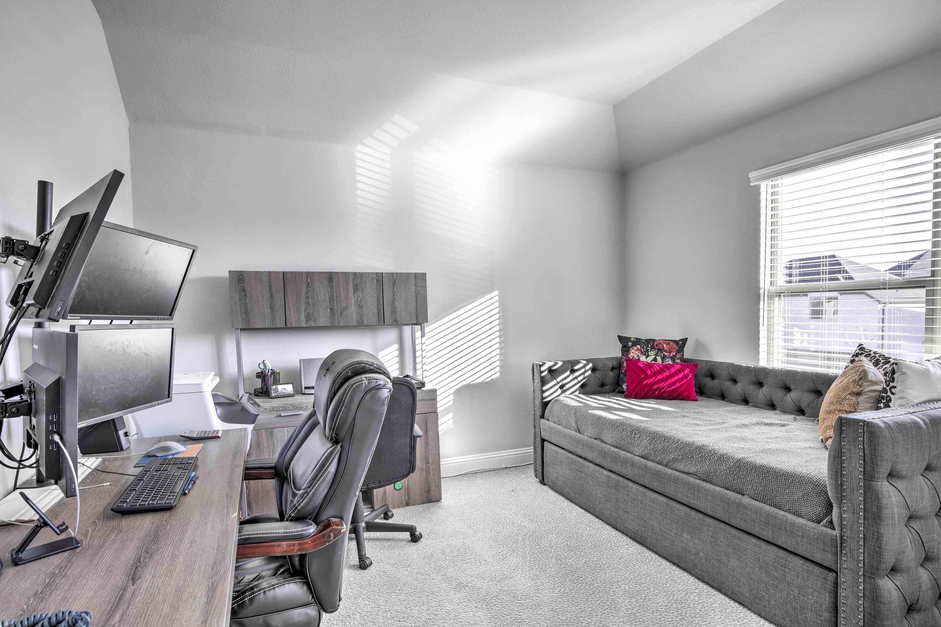 A modern office space with a desk, computer, and office chair. There is a grey sofa with a cushion and a cat on it.