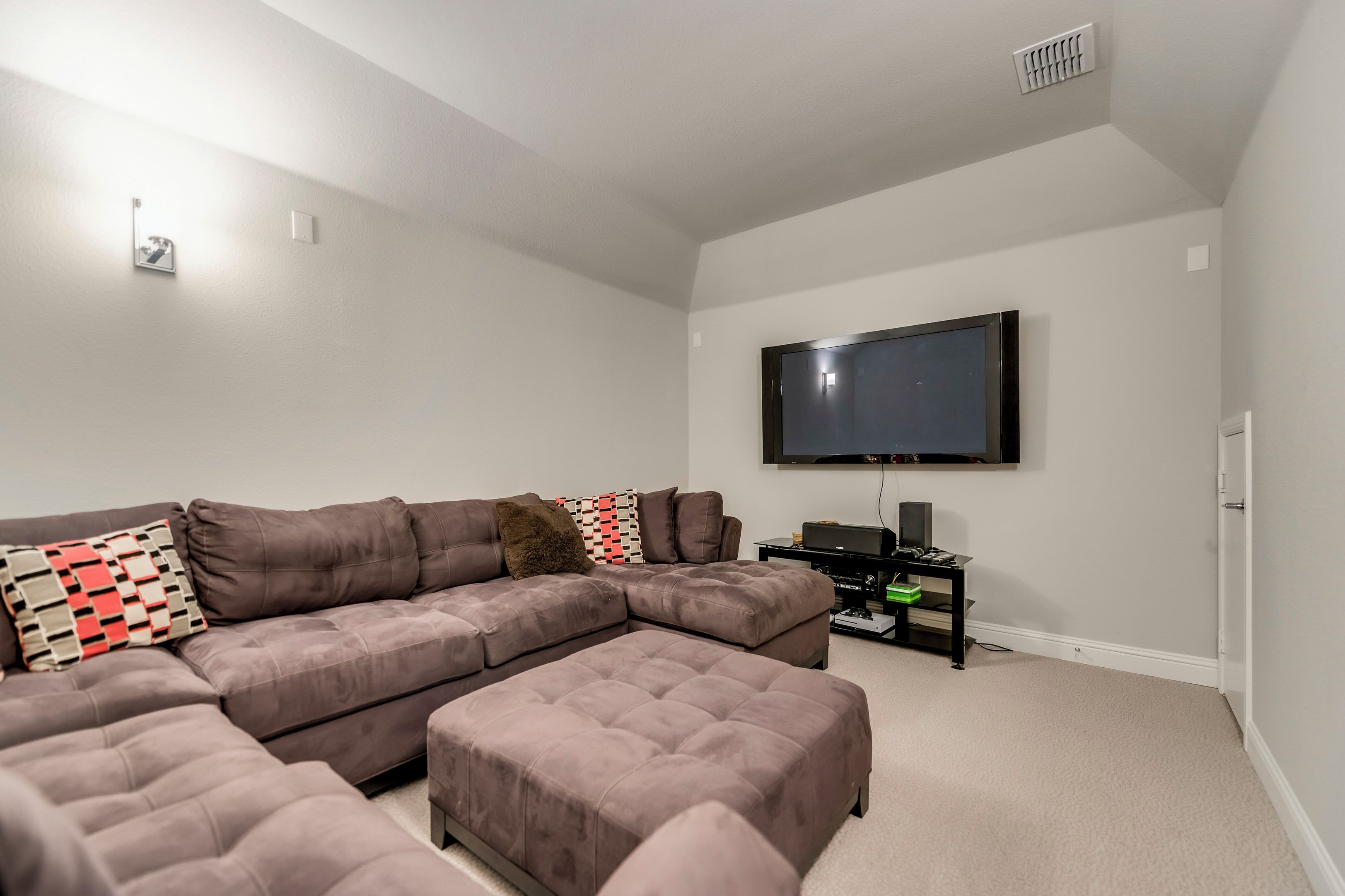A living room with a sectional sofa, ottoman, flat-screen TV, and a small black entertainment unit.