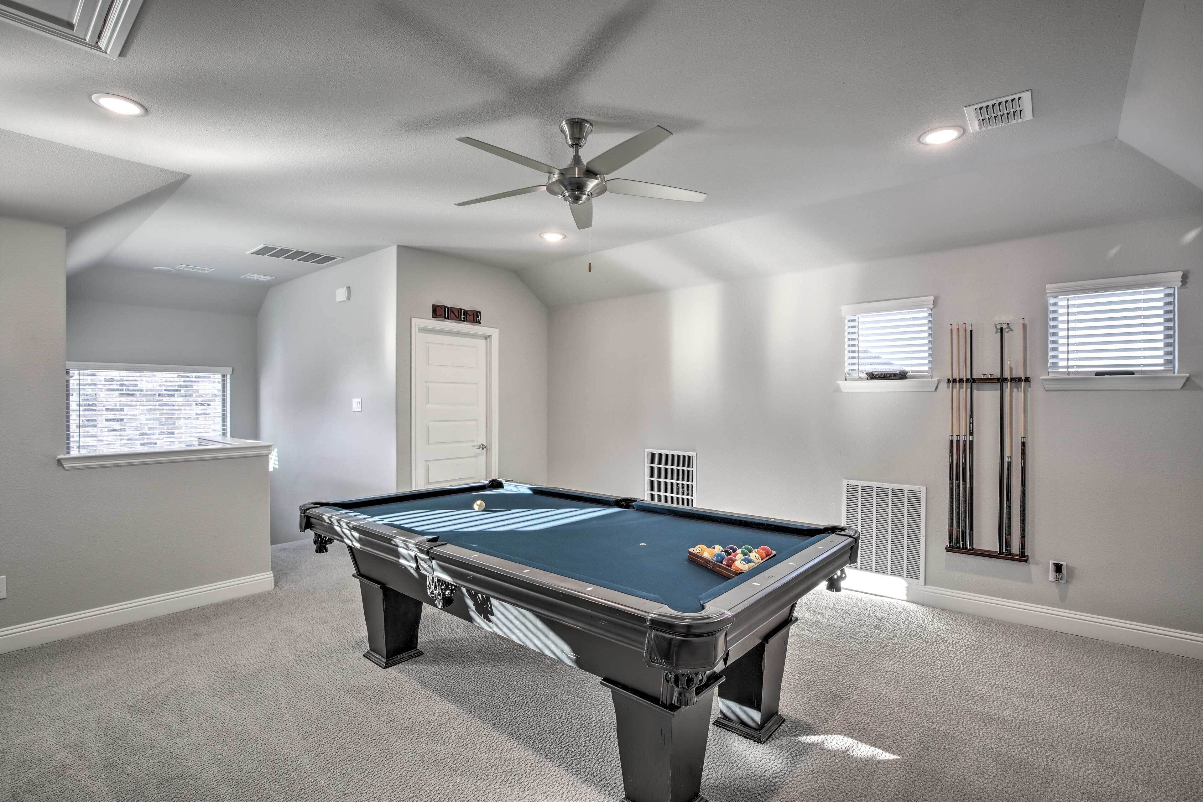 A pool table in a room with a ceiling fan, a door, and windows with blinds.