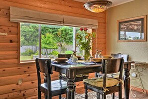 Un intérieur en bois avec une table à manger dressée pour quatre personnes, un vase rempli de fleurs et un luminaire décoratif au plafond, composé de vitraux.