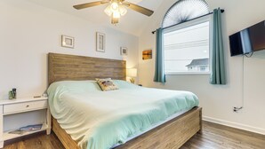 A bedroom with a wooden bed, a ceiling fan, a TV mounted on the wall, and a window with curtains.