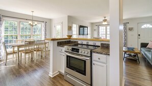 A spacious kitchen with a large stove, dining table, and chairs. There are large windows and a view of greenery outside.