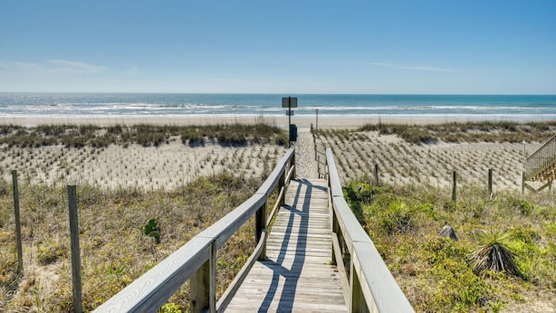 A wooden boardwalk leading to a beach with a clear view of the ocean.
