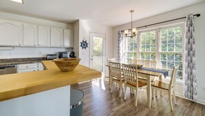 Una cocina moderna con armarios blancos, encimera de madera y comedor con mesa y sillas.
