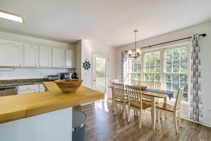 A modern kitchen with white cabinets, a wooden countertop, and a dining area with a table and chairs. - Topsail Beach Vacation Rental: Idyllic Ocean Views (Holly Ridge)