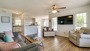 A spacious living room with a wooden floor, a ceiling fan, and a TV mounted on the wall.