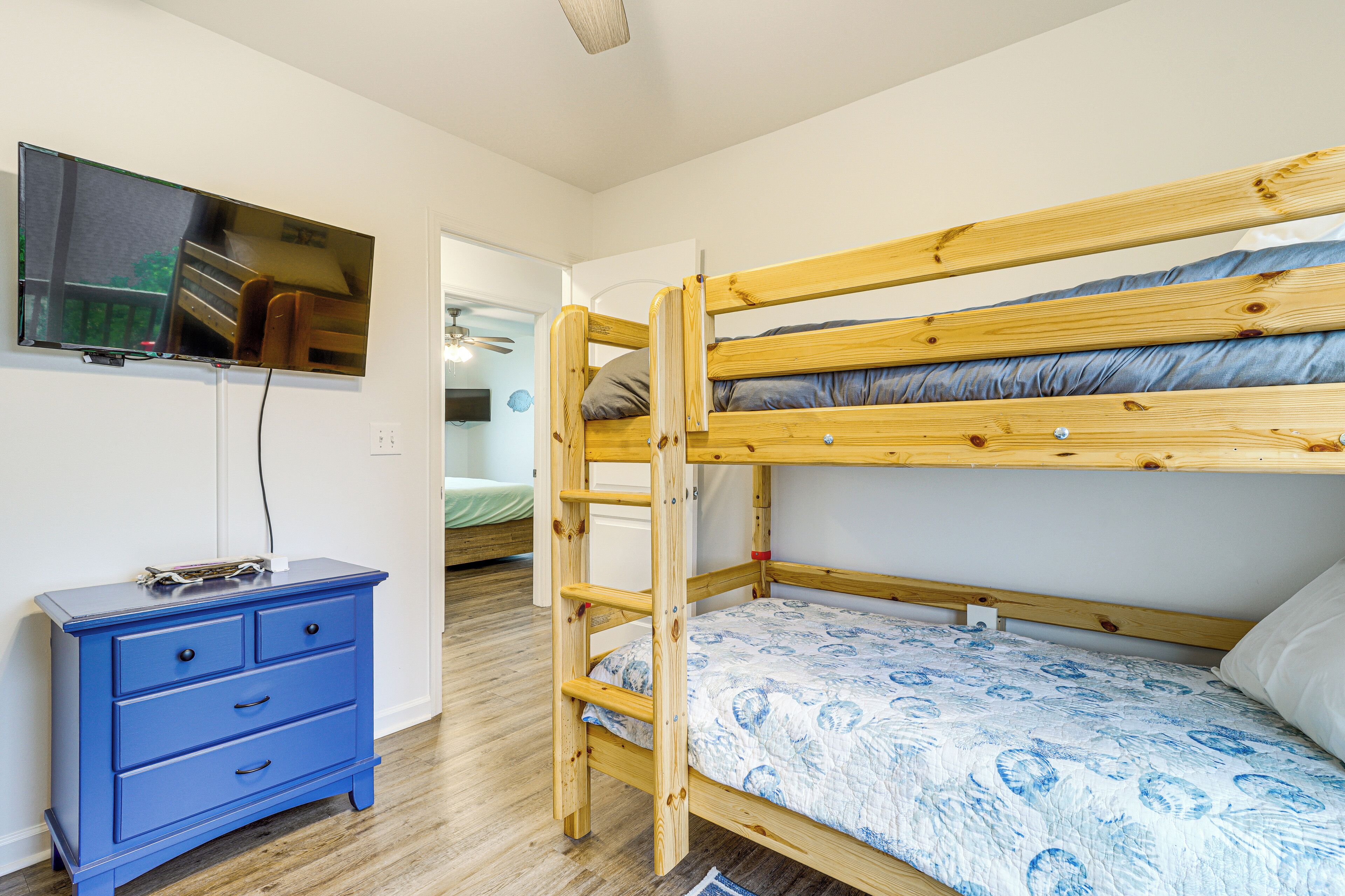 Ein Etagenbett mit Holzrahmen, eine blaue Kommode mit Schubladen und ein Flachbildfernseher an der Wand.