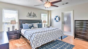 Une chambre à coucher comprenant un lit, des tables de chevet, une commode, un ventilateur de plafond et des œuvres d’art décoratives murales.