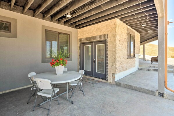 A patio area with a round table and chairs, a potted plant, and a view of a building with a brick facade and glass doors. - Newly Built Tooele Suite w/ Stunning Views! (Tooele)