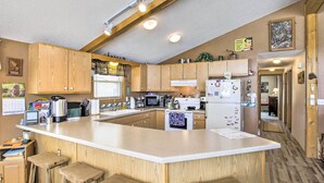 Une cuisine avec des meubles de rangement en bois, un grand îlot central doté de tabourets, un four à micro-ondes et un réfrigérateur.