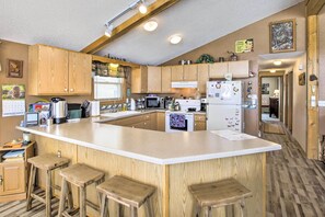 Une cuisine avec des meubles de rangement en bois, un grand îlot central doté de tabourets, un four à micro-ondes et un réfrigérateur.