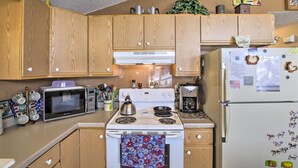 A kitchen with wooden cabinets, a microwave, stove, refrigerator, and various kitchen appliances. - Waterfront Friendship Home w/ Private Pier! (Friendship)