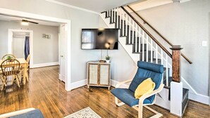 A living room with a wooden floor, a blue armchair, a small cabinet, and a staircase with a wooden railing. - Historic Staunton Home ~ 1 Mi to Downtown! (Staunton)