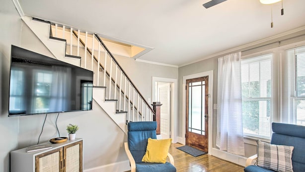 A living room with a staircase, a flat-screen TV, and two blue chairs with cushions. - Historic Staunton Home ~ 1 Mi to Downtown! (Staunton)