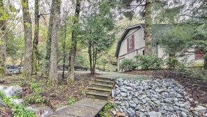 A wooden pathway leading to a rustic cabin surrounded by trees and a small stream.