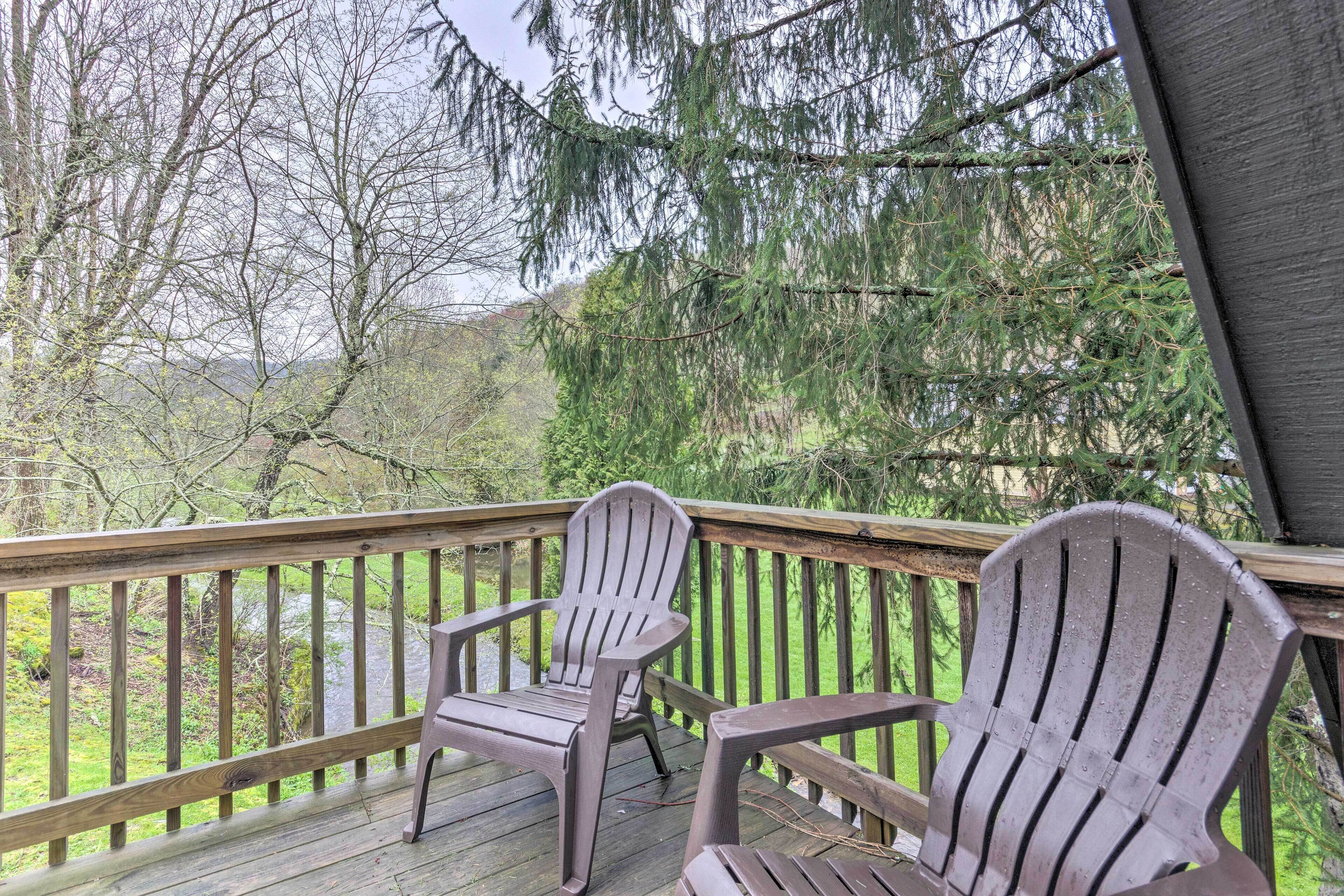 A wooden deck with two Adirondack chairs facing a natural landscape with trees and a river.