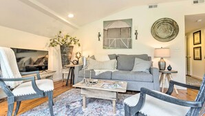 A living room with a grey sofa, two armchairs, a coffee table, a TV, and a decorative wall piece.