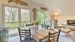 A dining area with a wooden table, chairs, and a view of the outdoors through large windows.