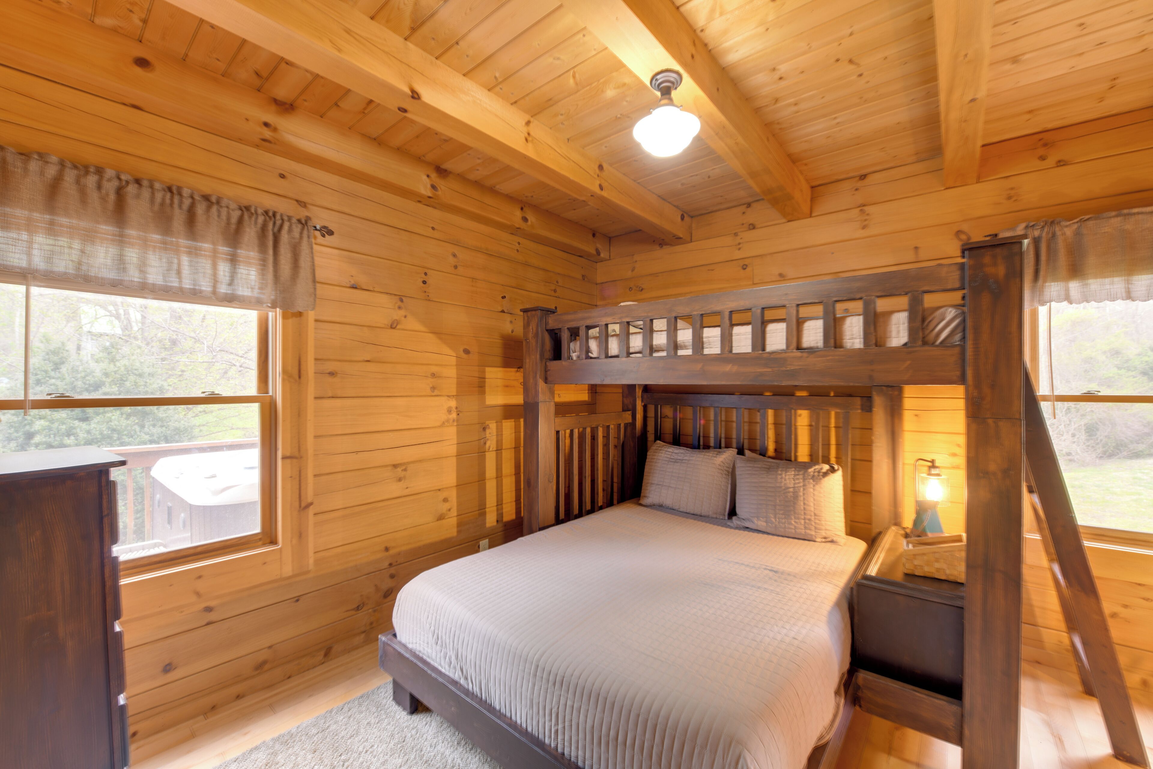 Un dormitorio de cabaña de madera con una cama litera, un escritorio y una ventana con cortinas.