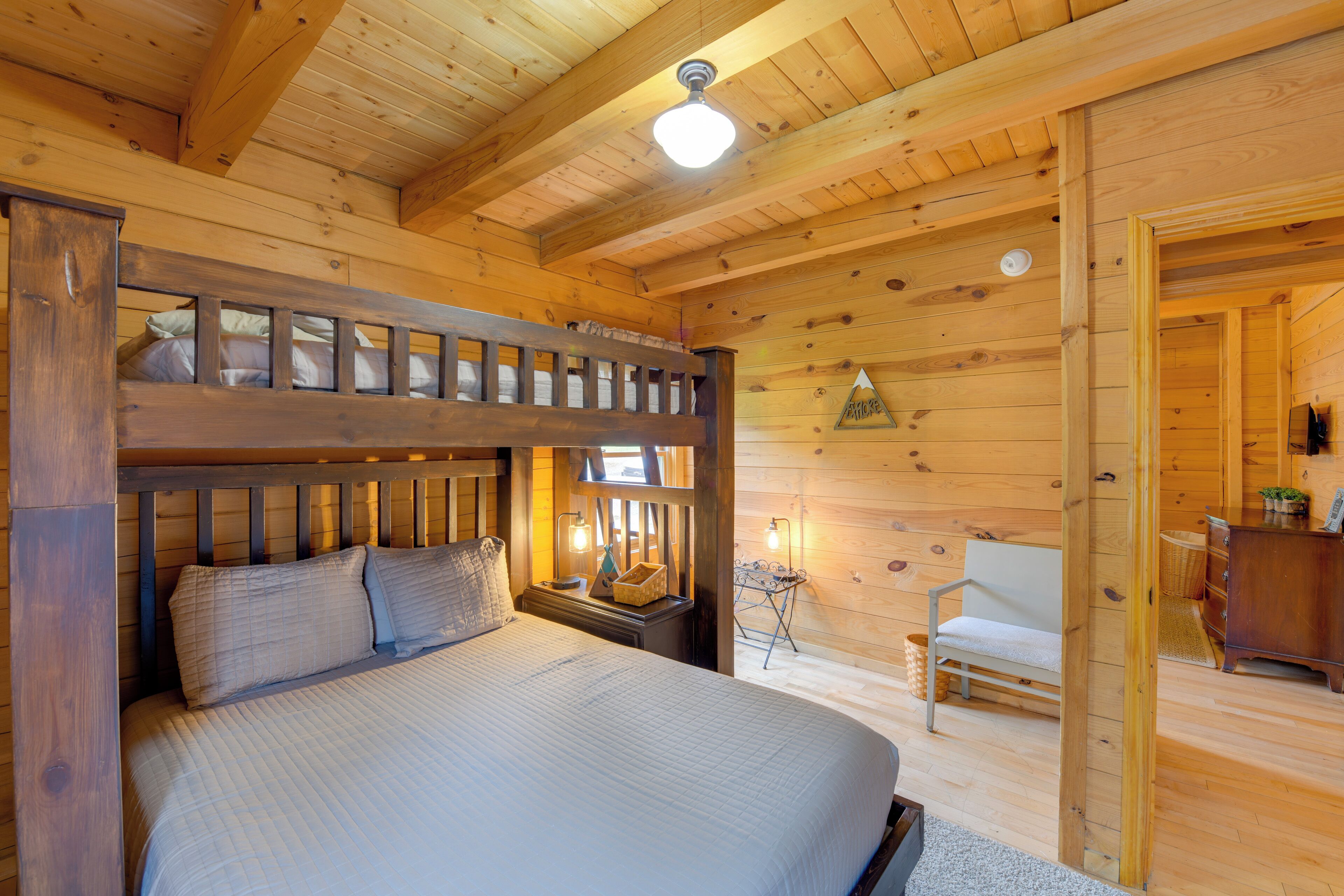 Camera da letto in una baita di legno con un letto a castello, un comodino con una lampada, una sedia e un piccolo tavolo con un cesto.