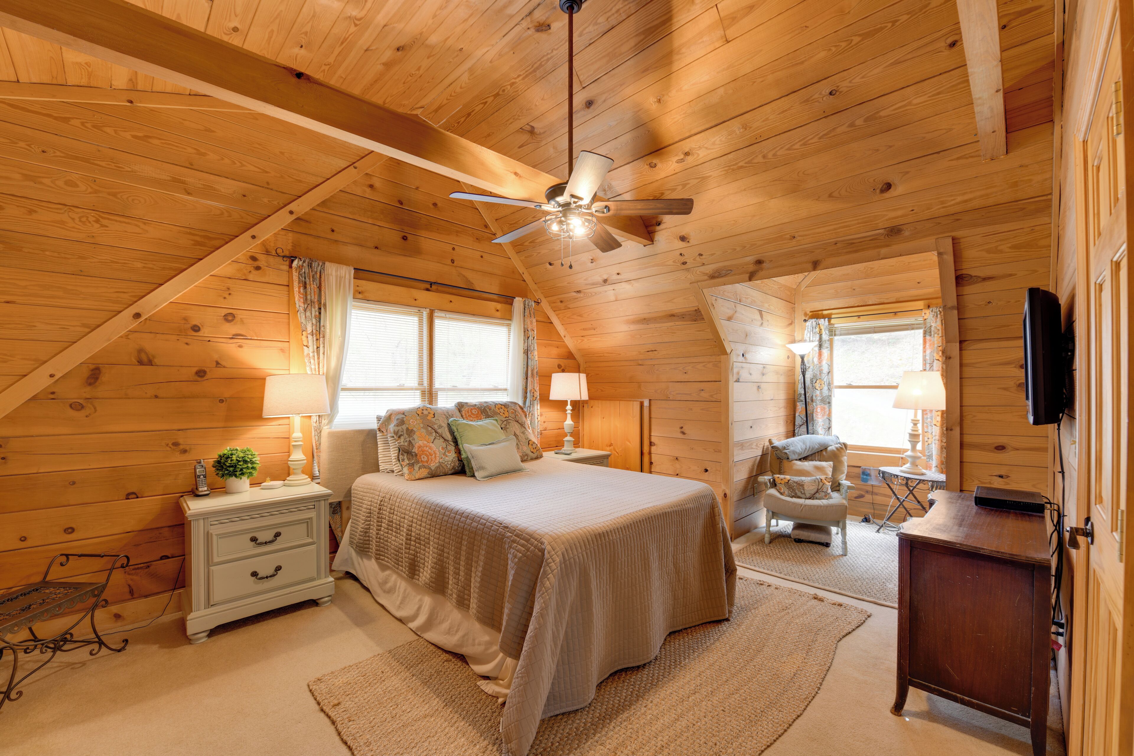 A cozy bedroom with a bed, nightstand, lamp, chair, and wooden walls.