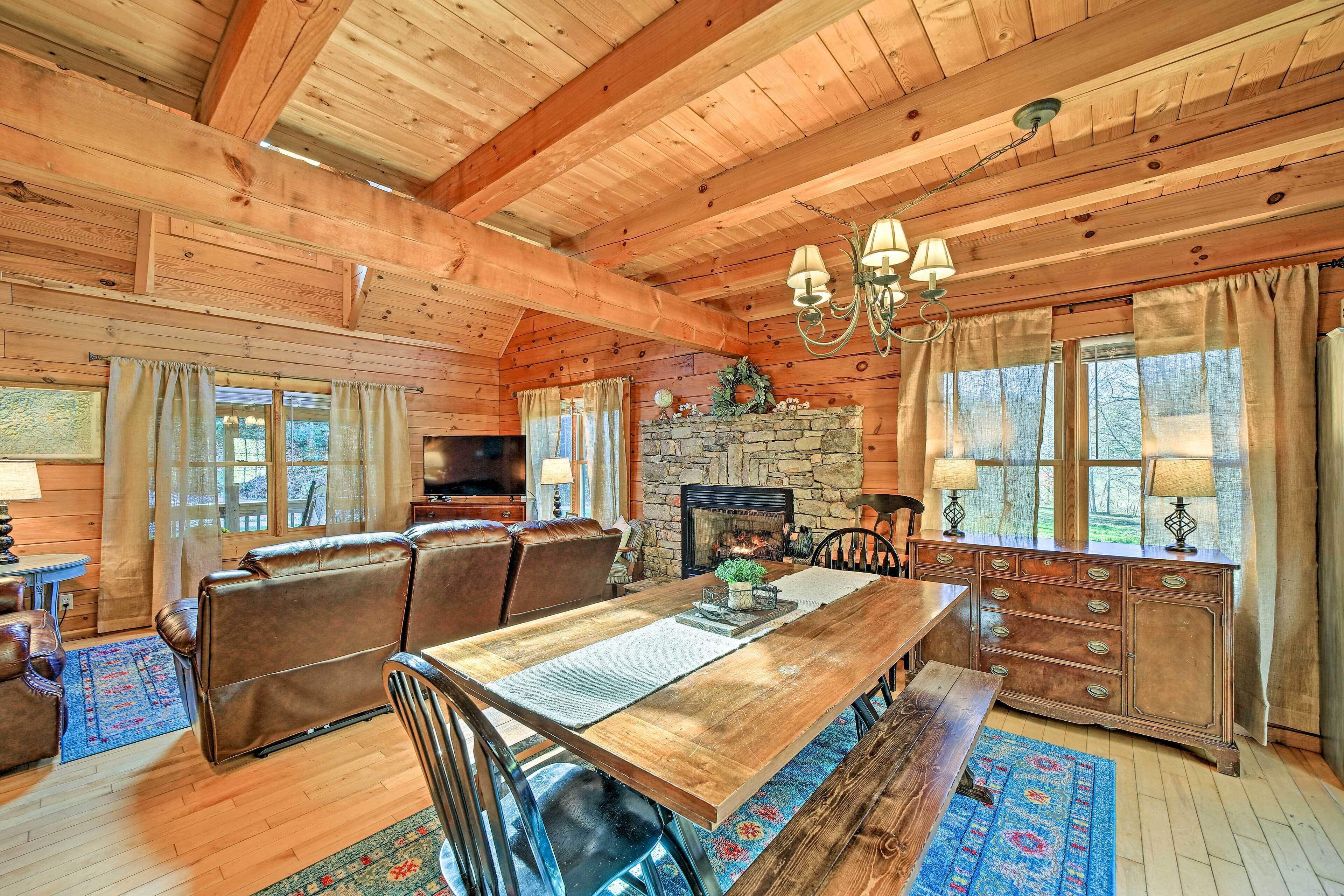 A wooden cabin interior with a dining area, fireplace, and stone wall.