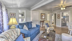 A spacious living room with a blue sofa, striped armchair, and a coffee table. There is a ceiling fan and a lamp on a side table. - Crescent City Apartment w/ Easy Lake Access! (Crescent City)