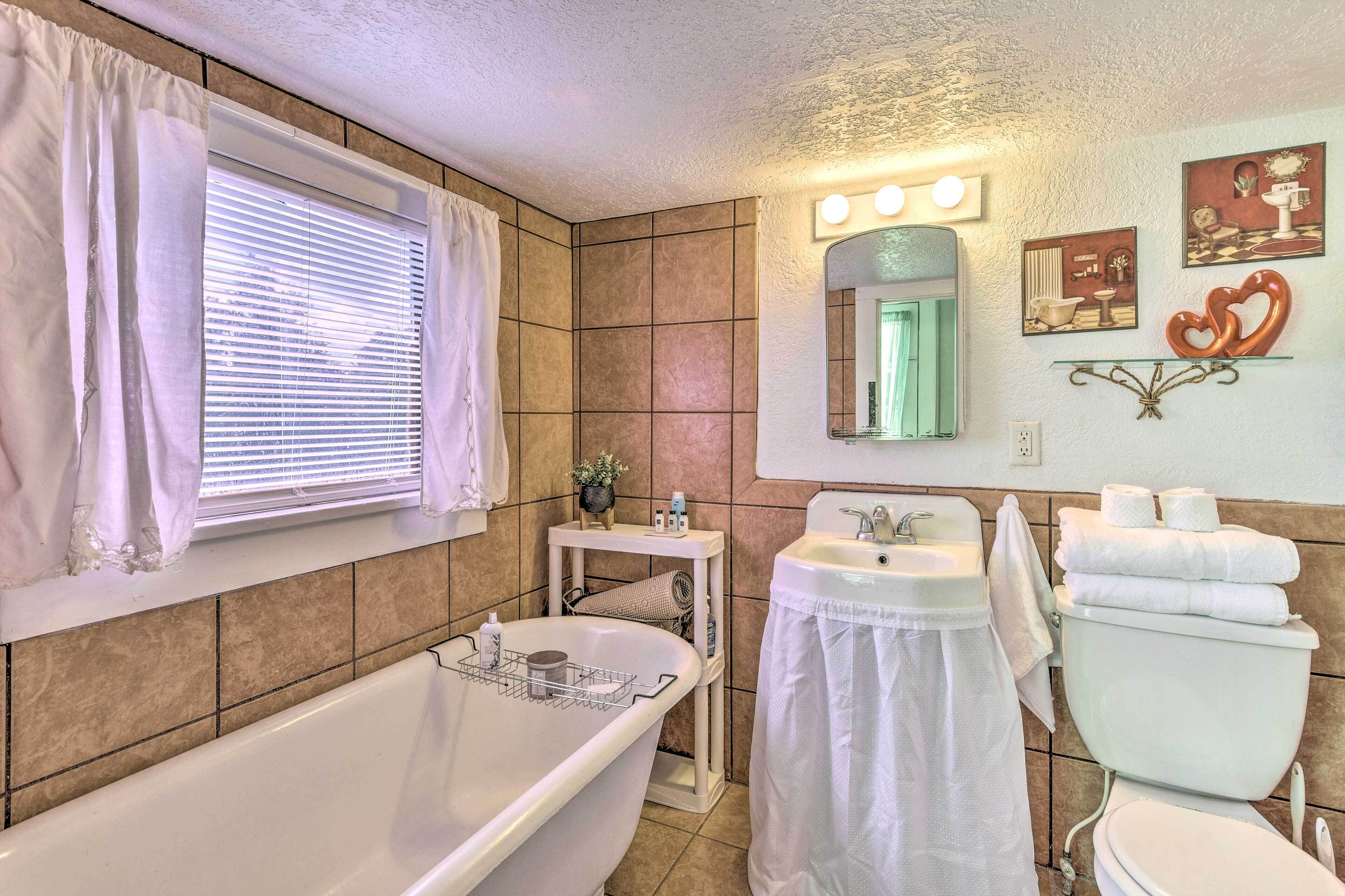 A bathroom with a bathtub, sink, toilet, vanity, and a window with curtains.