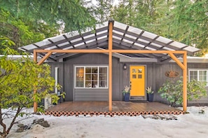 A house with a wooden deck, a yellow door, and a covered porch with a metal roof.