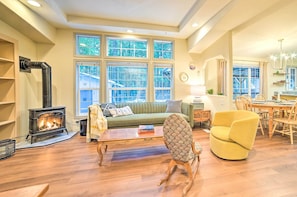 A cozy living room with a fireplace, a green sofa, a yellow armchair, and a dining area with wooden furniture.